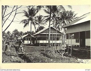 LAE, NEW GUINEA. 1944-03-29. QX6210 CAPTAIN L. B. SCHUBERT (FOREGROUND), AT THE 39TH SUPPLY DEPOT COMPANY. THE BUILDINGS COMPRISE THE SUPPLY OFFICE, HEADQUARTERS OFFICE, AND THE QUARTERMASTER'S ..