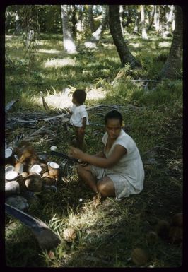 Young Tepou Marsters with George Iotua Marsters, breaking open coconuts for making copra, Palmerston Island