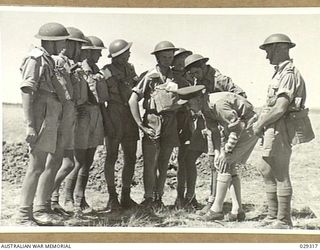 FORBES, NSW. 1943-02. MAJOR F.S. (FREDDIE) GORRILL, ROYAL ARMY MEDICAL CORPS, DEMONSTRATES TO THE "GUINEA PIGS" TAKING PART IN A GAS SHELL EXPERIMENT THE METHOD OF APPLYING PROTECTIVE OINTMENT TO ..