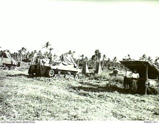 NEW IRELAND, 1945-10. A JAPANESE SERVICEMAN GUARDS A STORAGE AREA OF MIXED JAPANESE EQUIPMENT WHICH INCLUDES ARMOURED VEHICLES. (RNZAF OFFICIAL PHOTOGRAPH.)