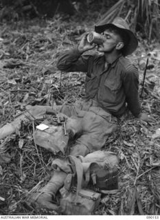 DAGUA, NEW GUINEA. 1945-03-27. PRIVATE W.T. LANE, 2/2 INFANTRY BATTALION (KILLED IN ACTION 1945-06-27), USING AN EMPTY MILK TIN AS A MUG. MOST UTENSILS ARE AT A COMPANY HEADQUARTERS AND IN THIS ..