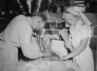 MADANG, NEW GUINEA. C. 1945. 500285 SISTER JOAN MESLEY ASSISTS MEDICAL OFFICER 241691 SQUADRON LEADER J. ISBISTER OF NORTH SYDNEY, NSW, AS HE EXAMINES A PATIENT AT NO. 1 MEDICAL RECEIVING STATION ..