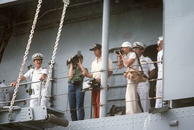 Photographers and crewmen aboard the docked combat stores ship USS NIAGRA FALLS (AFS 3) observe welcoming activities for the ship. The NIAGARA FALLS has just arrived at Naval Station Guam