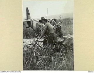 DAGUA, NEW GUINEA. 1945-03-25. SX29388 PRIVATE C.E. PUSH, 2/2 INFANTRY BATTALION, RIDES AN ABANDONED JAPANESE CYCLE ALONGSIDE THE WRECKAGE OF A JAPANESE FIGHTER