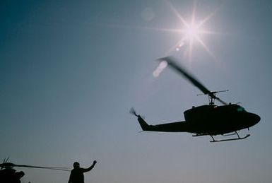 A silhouetted right side view of a UH-1 Iroquois helicopter in flight above the amphibious assault ship USS GUAM (LPH 9) during operations off the coast of Beirut, Lebanon