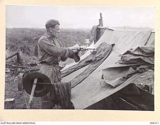 MOLONEY'S RIDGE, WEWAK, NEW GUINEA. 1945-07-13. SERGEANT S.J.A. SHIELDS, A COMPANY, 2/5 INFANTRY BATTALION, APPLYING ANTI-MITE SOLUTION TO HIS CLOTHES