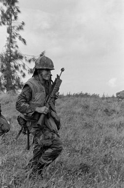 Private First Class Thompson of Company E, Battalion Landing Team, 2nd Bn., 3rd Marines, Marine Corps Air Station, Kaneohe Bay, armed with an M16A1 rifle mounted with an M-203 grenade launcher, advances toward his objective during a combat readiness evaluation exercise