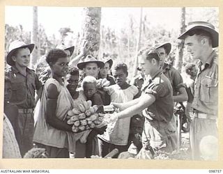 RABAUL, NEW BRITAIN. 1945-11-10. AN AUSTRALIAN SOLDIER BARTERING BULLY BEEF FOR A BUNCH OF BANANAS AT THE NATIVE MARKET AT TALILI BAY