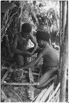 Pig festival, wig ritual, Tsembaga: man with wig frame in his hair builds fire
