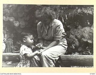 BASU RIVER VALLEY, NEW GUINEA. 1944-05-14. ONE OF SETO KONG'S SONS (1), EXAMINES A CIGARETTE LIGHTER HELD BY ELAINE CHAPMAN, AN AMERICAN RED CROSS SOCIETY REPRESENTATIVE (2), WHO IS VISITING A ..