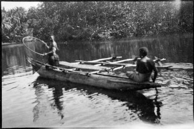 One seated person paddling in the stern and one standing person holding a fishing basket in the prow, Awar, Sepik River, New Guinea, 1935 / Sarah Chinnery