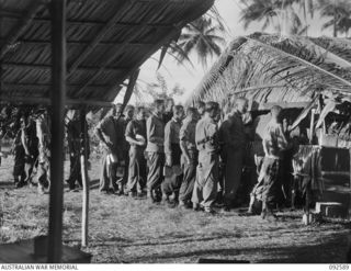 SAPOSA ISLAND, SOUTH BOUGAINVILLE. 1945-05-26. MEMBERS OF 42 LANDING CRAFT COMPANY LINING UP FOR MESS AT A NATIVE BUILT COOKHOUSE