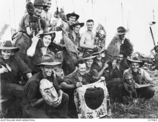 Alexishafen, New Guinea. 1944-04. Australian troops after the capture of Alexishafen with the spoils of war and barter - a Japanese flag and native carvings