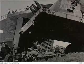 Lae, New Guinea. 27 October 1943. In a frame made by the open bows of a beach landing craft and giant road-making machinery, artillery and jeeps move out across a beach north-west of Lae. This is ..