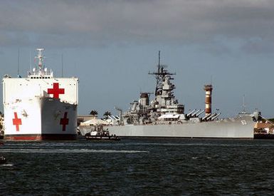 A bow on view showing the US Navy (USN) Military Sealift Command (MSC) Hospital Ship, USNS MERCY (T-AH 19) (left) being assisted by a tugboat as it arrives in port at Naval Base Pearl Harbor, Hawaii (HI), prior to deploying tp Southeast Asia to provide assistance to victims of the devastating Tsunami that hit the region in support of Operation UNIFIED ASSISTANCE. The USS MISSOURI (BB 63) Memorial is visible in the background