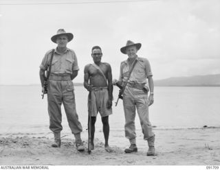 CAPE WOM, WEWAK AREA, NEW GUINEA. 1945-05-06. WARRANT OFFICER 2 H. WALBY (1), AND LIEUTENANT J.A. BIRRELL (2), AUSTRALIAN NEW GUINEA ADMINISTRATIVE UNIT PATROL OFFICERS, WITH MANUS, A NATIVE BOY ON ..