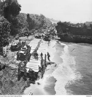 LAE, NEW GUINEA. 1943. UNITED STATES TROOPS LAYING METAL STRIPS ALONG THE BEACH DURING THE UNLOADING OF SUPPLIES AND MOTOR VEHICLES FROM LANDING SHIPS