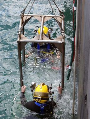 US Navy (USN) Divers from Mobile Diving and Salvage Unit One (MDSU-1) use a diving stage to conduct training dives alongside the Crowley 450 Barge, in preparation for recovery operations for the Japanese fishing vessel Ehime Maru