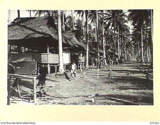 MILNE BAY, NEW GUINEA, 1944-02-10. MOSES, SUPERVISOR OF 1800 NATIVE LABOURERS, INSPECTS NATIVE CARPENTERS AT HEADQUARTERS, BARAGA NATIVE LABOUR CAMP. THE HUTS ARE QUARTERS OF THE AUSTRALIAN NEW ..