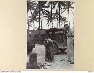 PALMALMAL PLANTATION, JACQUINOT BAY, NEW BRITAIN, 1945-08-15. PRIVATE P. MCILLROY (1), REPAIRING A PUNCTURED TYRE AT 33 DOCKS OPERATING COMPANY ROYAL AUSTRALIAN ENGINEERS. HE IS WATCHED BY CAPTAIN ..