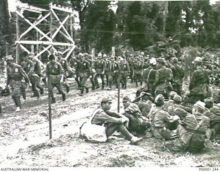 THE SOLOMON ISLANDS, 1945-09-19. SOME JAPANESE TROOPS FROM NAURU ISLAND REST AS THEY WATCH FELLOW SERVICEMEN ENTERING THEIR INTERNMENT CAMP ON BOUGAINVILLE ISLAND AFTER MARCHING FROM TOROKINA. ..