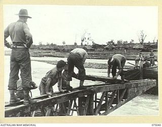 LAE, NEW GUINEA. 1944-08-09. TROOPS OF THE 20TH FIELD COMPANY, "NOSING" THE FIRST SPAN OF A NEW BRIDGE ACROSS THE BUTIBUM RIVER WHICH IS TO REPLACE THE OLD ONE WHICH WAS WASHED AWAY DURING THE ..