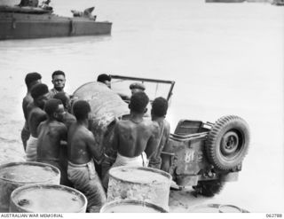 SIALUM BEACH, NEW GUINEA. 1944-01-08. NATIVES LOADING 44 GALLON DRUMS OF PETROL AND OIL ONTO A JEEP