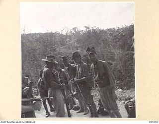 MOUNT SHIBURANGU, WEWAK AREA, NEW GUINEA. 1945-09-21. AN AUSTRALIAN OWEN GUNNER OF HEADQUARTERS 6 DIVISION COVERING JAPANESE SOLDIERS OF 18 JAPANESE ARMY WHO ARE PASSING IN WEAPONS AT A CONTROLLING ..