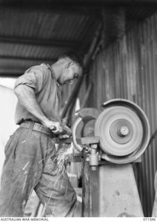 LABU POINT, LAE, NEW GUINEA. 1944-03-24. NX32050 CRAFTSMAN A. F. WATT SHARPENING A CHISEL IN THE COPPERSMITH'S SHOP AT THE 1ST WATERCRAFT WORKSHOP