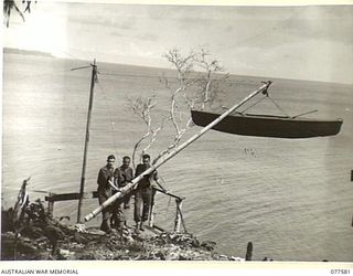 TROOPS OF THE 27TH INFANTRY BATTALION BESIDE THE LIFTING GEAR WHICH THEY HAVE RIGGED UP IN ORDER TO LOWER THEIR SAILING CRAFT INTO THE WATER AT THE FOOT OF THE CLIFF NEAR THEIR CAMP. IDENTIFIED ..