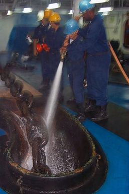 Sailors aboard the amphibious assault ship USS SAIPAN (LHA 2) spray down the anchor chain on the forecastle during sea and anchor detail