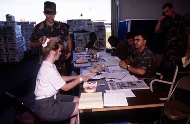 Air Force personnel assist a woman in filling out forms during evacuation processing. The evacuation is the result of the June 10 eruption of Mount Pinatubo, which deposited more than four inches of volcanic ash on the Philippine Islands. More than 20,000 evacuees have been removed from the area as a part of the U.S. military's Operation Fiery Vigil