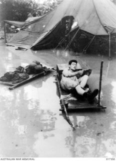 Northern New Guinea. 1944-06. Torrential rain flooded many United States 6th Army men out of their tents. Private Walter Koch of Ohio, USA, disregards the water and relaxes on his stretches with a ..