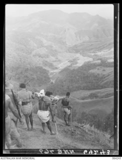 FINISTERRE RANGES, NEW GUINEA. 1944-01-23. NATIVES CARRYING A STRETCHER CASE DOWN A STEEP SLOPE FROM SHAGGY RIDGE, ON THE WAY TO THE ADVANCED DRESSING STATION AT GUY'S POST. IN THE CENTRE OF THE ..