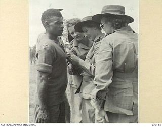 LAE, NEW GUINEA. 1944-09-12. NURSES FROM THE 2/7TH GENERAL HOSPITAL ADMIRING THE BRITISH EMPIRE MEDAL, (CIVIL DIVISION), AWARDED TO GOMERI (1) BY LIEUTENANT GENERAL S. G. SAVIGE, CB, CBE, DSO, MC, ..