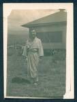 Don Honeysett dressed in a robe standing in front of a house, New Guinea, c1929 to 1932