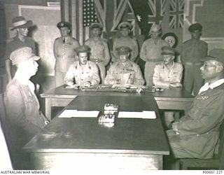 THE SOLOMON ISLANDS, TOROKINA, BOUGAINVILLE ISLAND, 1945-09-08. LIEUTENANT GENERAL SIR STANLEY SAVIGE, (GOC II AUSTRALIAN CORPS), SEATED AT CENTRE OF TABLE CHECKS THE TERMS OF SURRENDER DOCUMENT; ..