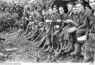 WARAPA AREA, BOUGAINVILLE ISLAND. 1945-02-13. TROOPS OF THE 61ST INFANTRY BATTALION SEATED ON A LARGE TREE FALLEN BY THE JAPANESE AS A ROAD BLOCK, WHILE ENJOYING A CUP OF TEA ON THEIR RETURN FROM A ..