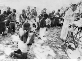 Reverend Father Tom Ormonde celebrates Mass on the beach at Puto.  The rough altar was built by the native altar boys assisting Father Ormonde and soldiers from the 31/51 Battalion gather around.  ..