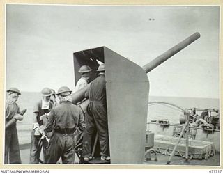 The gun crew firing the 4 inch Mark XIX gun on a Mark XXIII mounting aboard the RAN Corvette Geelong, while on convoy duty off the New Guinea coast