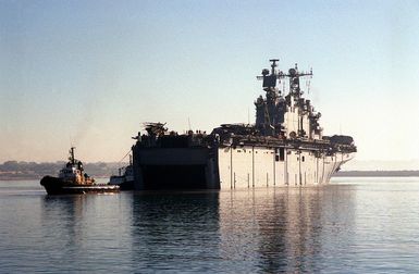 A starboard view of the stern of the TARAWA CLASS AMPHIBIOUS ASSAULT SHIP USS SAIPAN (LHA 2) as it gets a tow entering the harbor at Naval Station Rota, Spain. The SAIPANS crew will assist in wash-down and inspection of all land vehicles onboard ship during the port visit