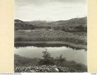 WAU - LAE ROAD, NEW GUINEA, 1944-02-26. LOOKING NORTH EAST ACROSS THE WATUT VALLEY TOWARDS THE MOUNTAINS. IN THE FOREGROUND IS A DREDGE HOLE EDGED BY DREDGE TAILINGS. THE ROAD IN THIS AREA IS ..