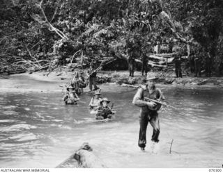 Members of B Company, 30th Infantry Battalion, crossing the river near Weber Point in the advance over muddy swamps, kunai grass, and innumerable rivers from Roinji to link with American troops at ..