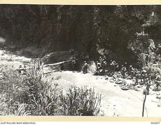 FARIA RIVER, NEW GUINEA. 1944-01-20. MEMBERS OF THE 2/5TH FIELD AMBULANCE CROSSING THE FARIA RIVER BELOW THE PLATEAU. THIS UNIT IS MOVING INTO POSITION IN PREPARATION FOR THE CASUALITIES DURING THE ..