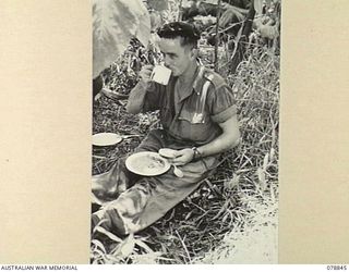 BOUGAINVILLE ISLAND. 1945-01-31. N165380 PRIVATE L.E. BEAUMONT, "B" COMPANY, 9TH INFANTRY BATTALION RELAXING IN THE SHADE OF A TREE WHILE ENJOYING A HOT MEAL