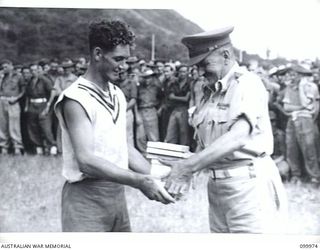 RABAUL, NEW BRITAIN, 1946-04-06. MAJOR-GENERAL B.M. MORRIS, GENERAL OFFICER COMMANDING 8 MILITARY DISTRICT, PRESENTING SIGNALMAN W.J. RALPH WITH TROPHIES FOR THE "OTHER STATES" AUSTRALIAN RULES ..