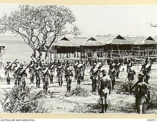 PORT MORESBY, PAPUA. 1942-07-20. MORNING PARADE IN A NEW SETTING. RIFLE INSPECTION FOR AUSTRALIAN INFANTRY IN A PAPUAN VILLAGE