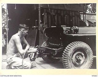 BOUGAINVILLE. 1945-08-30. CRAFTSMAN R. BEATTIE, 202 LIGHT AID DETACHMENT ATTACHED HEADQUARTERS 3 DIVISION, USING A SPRAY GUN, REDUCOING A JEEP. THE AIR COMPRESSOR AND TANK IS INSTALLED IN TRUCK IN ..