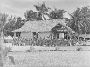 [Group portrait of young students standing outside school building]