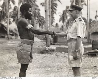 LUNGGA, GUADALCANAL, BRITISH SOLOMON ISLANDS PROTECTORATE. 1943-10-14. SERGEANT YAUWIKA OF THE NATIVE POLICE IS CONGRATULATED BY LIEUTENANT COMMANDER I. PRYCE-JONES RANVR, NAVAL INTELLIGENCE ..